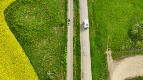 A-top-down-aerial-view-of-a-road-flanked-by-green-and-yellow-fields,-with-a-camper-driving-along-the-road