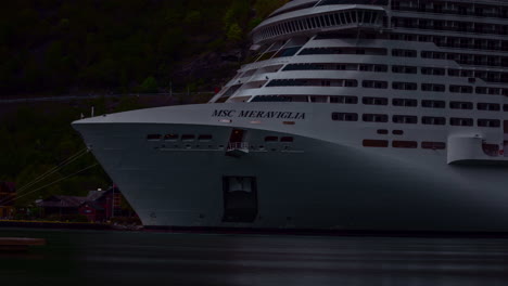 Big-white-cruise-ship-docked-at-harbor-in-Norway-Fjord,-sunlight-shining-on-vessel,-timelapse