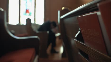 Young-man-in-black-suit-praying-in-church-in-cinematic-slow-motion-with-folded-hands-with-bible-in-pew