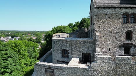 Medieval-Bedzin-castle-with-a-turret,-stone-walls,-and-courtyard-during-a-beautiful-summer-day-surrounded-by-lush-greenery,-under-a-clear-blue-sky