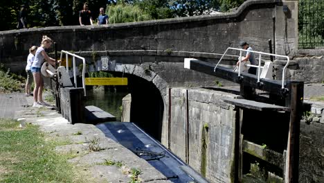 Old-English-narrowboat,-passing-through-the-canal-lift,-Broad-locks,-under-a-bridge