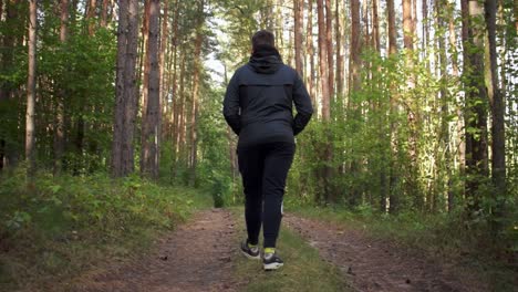 Scenic-tracking-shot-of-young-man-with-black-jacket-walking-on-a-path-through-the-forest-with-beautiful-sunlight