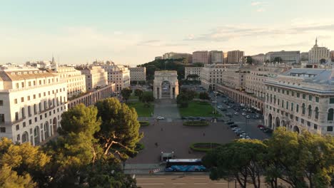 Piazza-della-vittoria-in-genoa-at-sunset-showcasing-grand-architecture-and-bustling-streets,-aerial-view