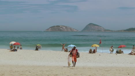 Worker-man-walking-to-sell-mate-tea-on-ipanema-beach-in-a-sunny-day