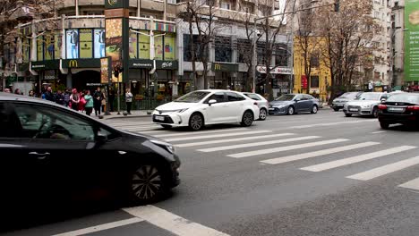 Busy-street-scene-in-Bucharest-with-cars-crossing-an-intersection-on-a-cloudy-day,-city-vibe