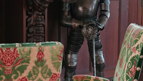 Close-up-of-a-suit-of-armor-with-gauntleted-hands,-flanked-by-richly-upholstered-floral-chairs-in-Trakoscan-Castle