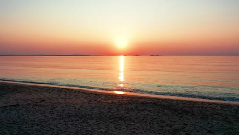 Vista-Del-Amanecer-En-El-Océano-Mientras-Camina-En-La-Playa-Con-Un-Sol-Brillante-Que-Proyecta-Coloridos-Reflejos-Rojos,-Naranjas,-Morados-Y-Amarillos-Sobre-Las-Tranquilas-Olas-Del-Mar-Con-Un-Hermoso-Cielo