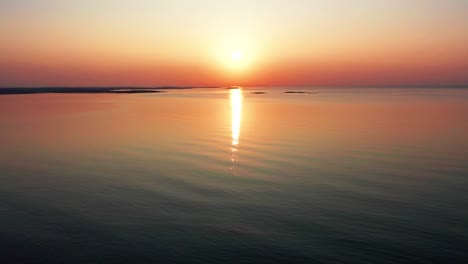 Wunderschöner-Sonnenaufgang-Am-Meer-Mit-Hell-Leuchtender-Sonne,-Die-Farbenfrohe-Rote,-Orange,-Violette-Und-Gelbe-Reflexe-Auf-Die-Friedlich-Plätschernden-Wellen-Des-Meeres-Wirft
