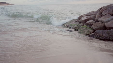 Sea-water-hitting-rocks-on-a-beach,-creating-gentle-waves-and-splashes
