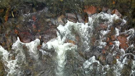 Wasser-Fließt-Flussabwärts-über-Glatte-Flussfelsen,-Die-Mit-Kalktünche-Verwirbelt-Sind