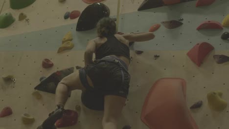 Woman-climbing:-Female-climber-ascending-indoor-rock-wall-with-colorful-holds