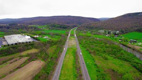 Aerial-view-of-highway-with-semi-trucks-in-Milesburg,-PA-surrounded-by-green-landscapes