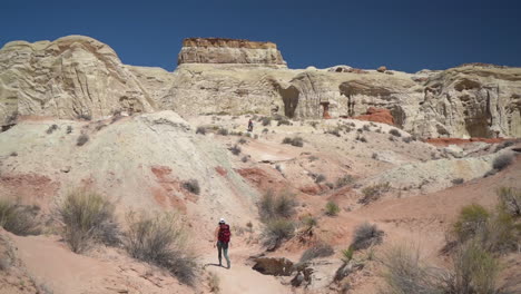 Lonely-Female-Hiker-With-Backpack-Walking-on-Desert-Hiking-Trail-Under-Sandstone-Formations-on-Hot-Sunny-Day