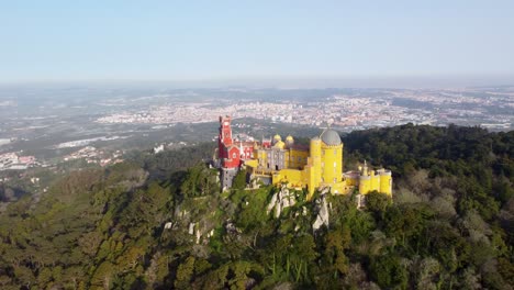 Farbenfroher-Pena-Palast-In-Sintra,-Portugal,-Bremsrampe-Zurück-In-Weite-Landschaft:-Luftaufnahme-Von-Drohnen,-Helles-Schloss-In-Der-Nähe-Von-Lissabon,-Strahlend-Sonniger-Tag