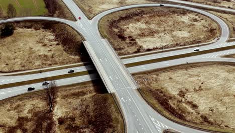 Roundabout-countryside-road,-cars-driving-along-dry-earthy-landscape,-aerial-drone-panoramic-view,-asphalted-ways-junction