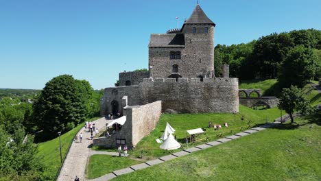 Medieval-castle-with-a-turret,-white-stone-walls,-and-courtyard-during-a-beautiful-summer-day-surrounded-by-lush-greenery,-under-a-clear-blue-sky