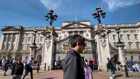 People-stroll-in-front-gates-of-Buckingham-Palace-on-a-sunny-morning-in-London,-England,-capturing-the-vibrant-city-life-and-the-allure-of-iconic-landmarks