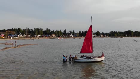 Luftaufnahme-Von-Menschen,-Die-Am-Frühen-Abend-Auf-Dem-Fluss-Ein-Segelboot-Besteigen