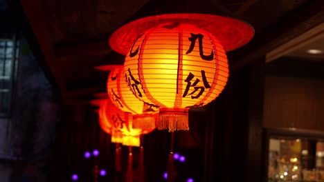 Traditional-Chinese-red-lanterns-with-Jiufen-character-print,-swaying-gently-in-the-dark-night,-casting-a-warm-glow-against-the-dark-backdrop,-close-up-shot