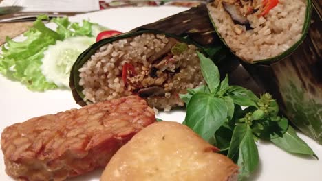 Pan-shot-of-grilled-rice-wrapped-in-banana-leaves-on-a-plate-with-various-interesting-side-dishes