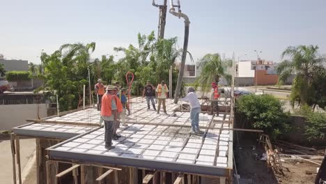 Aerial-above-roof-pouring-cement-to-build-roof-or-floor-structure-wearing-orange-vests-as-construction-workers-working-on-site