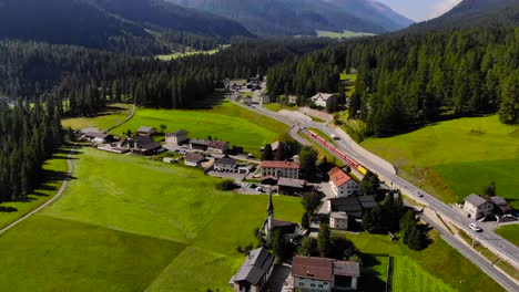 Aerial:-train-by-an-alpine-town-in-a-mountainous-landscape