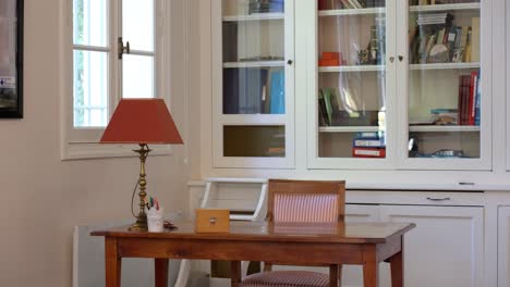 Langsame-Einstellung-Eines-Kleinen-Heimbüros-Mit-Einem-Bücherregal-Aus-Glas-Dahinter