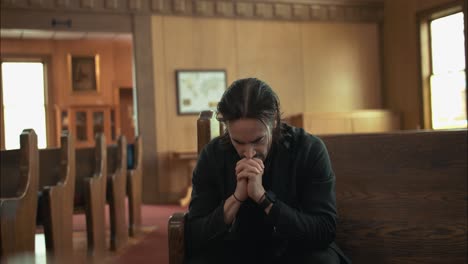 Young-man-in-black-suit-praying-in-an-old-church-in-cinematic-slow-motion