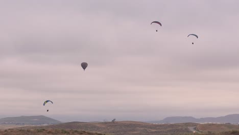 Temecula-Balloon-and-Wine-Festival-Drone-View-of-Hot-Air-Balloon-surrounded-by-three-active-paragliders-two-of-which-leave-frame-to-the-right