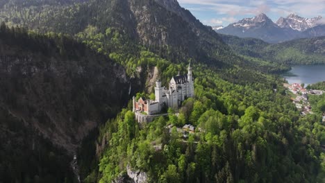 Aerial-Circling-Shot-of-White-Castle-in-Middle-of-Green-Mountain-Forest,-Lake-in-Background,-Beautiful-Scenery