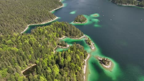 Aerial-showcasing-Eibsee's-intricate-shoreline-with-emerald-green-waters-and-densely-forested-islands-in-Grainau,-Germany