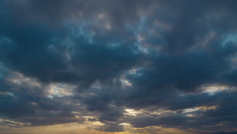 Sunset-cloudscape-with-vivid-blues-and-grays,-highlighted-by-a-golden-sun-peeking-through