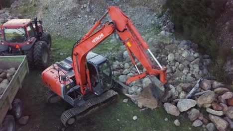 New-Zealand's-Hitachi-Excavator-Machine-Grabbing-Rocks-From-A-Rocky-Hillside-And-Loading-Them-To-A-Rock-Truck---high-angle-shot