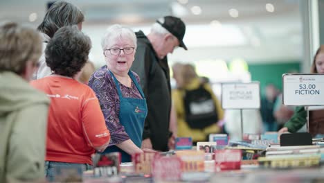 An-Older-Woman-Exhales-Supirsed-Looking-Overwhelmed-at-a-Used-Book-Sale-in-a-Mall