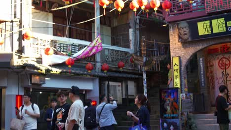 Tilt-up-shot-of-Jiufen-Old-Street's-bustling-square,-featuring-the-Ghost-Lore-Museum-and-red-lanterns-hanging-above-the-plaza,-a-popular-tourist-spot-nestled-in-Taiwan's-mountain-town