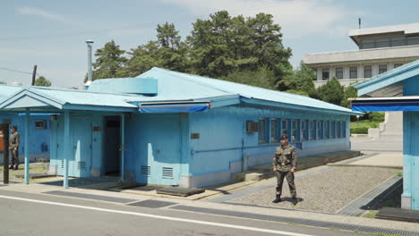 Truce-Village-in-the-Joint-Security-Area-of-the-Korean-Demilitarized-Zone-with-South-Korean-soldier-standing-guard,-wide-pan-right-in-slow-motion