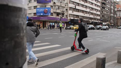 Man-crossing-a-street-in-Bucharest-on-a-cloudy-day,-urban-traffic-and-pedestrians-around