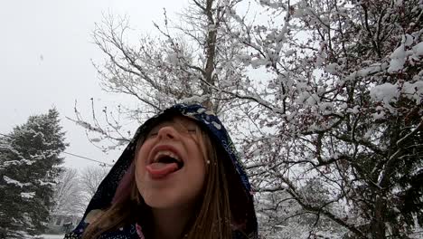 Young-Girl-Enjoying-Winter-Outdoors-Catching-Snowflakes-With-Her-Tongue-Out-On-Snowy-Trees-Background-In-Michigan,-USA---Slow-Motion