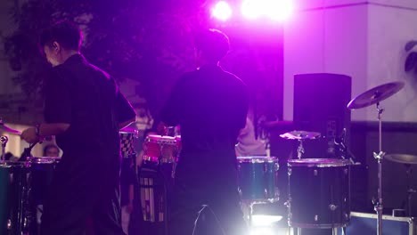 Two-young-Asian-man-hitting-drum-plates-and-cymbals-on-a-stage-under-spotlight-at-night