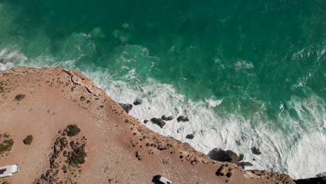 Drone-view-of-tall-towering-cliffs-with-waves-crashing-against-the-rocks-below