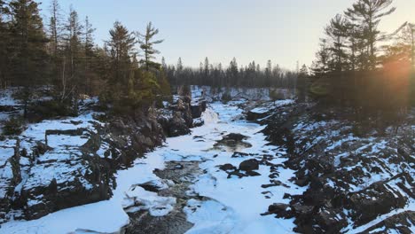 Aerial-view-snowy-river-in-middle-of-forest-in-a-sunset