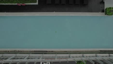 Luftaufnahme-Eines-Swimmingpools-Auf-Dem-Dach-Mit-Liegestühlen-Und-Grünflächen,-Gelegen-über-Einer-Stadtstraße-Mit-Autos
