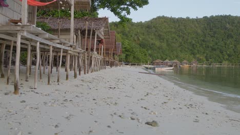 Wooden-huts-on-the-sandy-beach-in-Kri-Island-in-the-Raja-Ampat-Archipelago-of-Indonesia,-marred-by-the-unfortunate-sight-of-two-plastic-bottles-littering-the-pristine-landscape