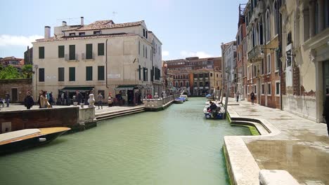 Scenic-view-of-a-canal-with-italian-architectural-buildings-and-tourists-walking-around-in-Venice