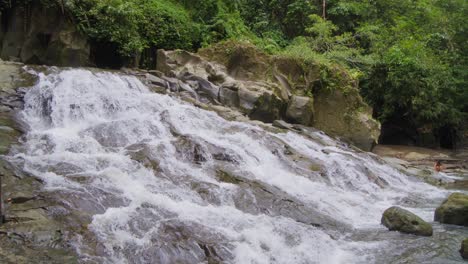 Woman-sits-in-waters-of-Goa-Rang-Reng-waterfall-on-Bali-island-in-Indonesia