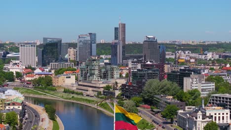 Aerial-Pullback-Reveals-Lithuanian-Flag-Above-Gediminas-Tower,-Modern-Skyscrapers-in-Background