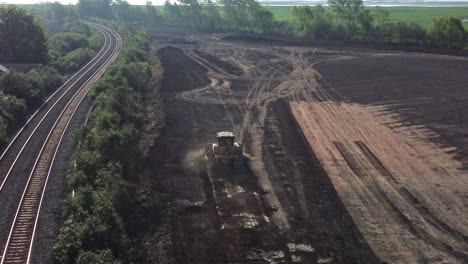 Aerial-view-overlooking-bulldozer-leaving-housing-construction-site-next-to-railway-tracks-in-the-early-morning-sunrise