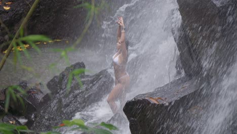 A-beautiful-woman-stands-under-the-cascading-waters-of-Kanto-Lampo-Waterfall-in-Bali,-Indonesia