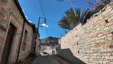 Upward-view-of-a-narrow-street-in-Lefkara-with-stone-walls-and-palm-tree