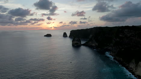 Sunsetting-over-dark-cliff-coastline,-Nusa-Penida,-Indonesia,-aerial